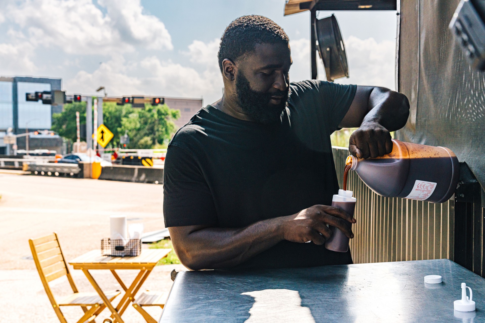 Black Food Truck Owner Man Filling a Condiment Squeeze Bottle with Sweet, Savory BBQ Sauce for outdoor lunchtime service in Houston Texas